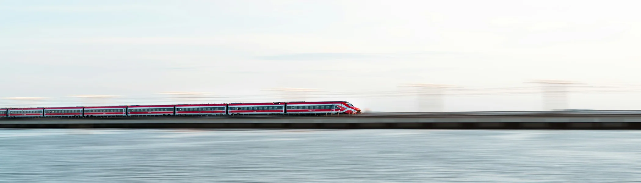 Red and white high-speed train crossing the causeway over the Venetian Lagoon toward Venezia Santa Lucia